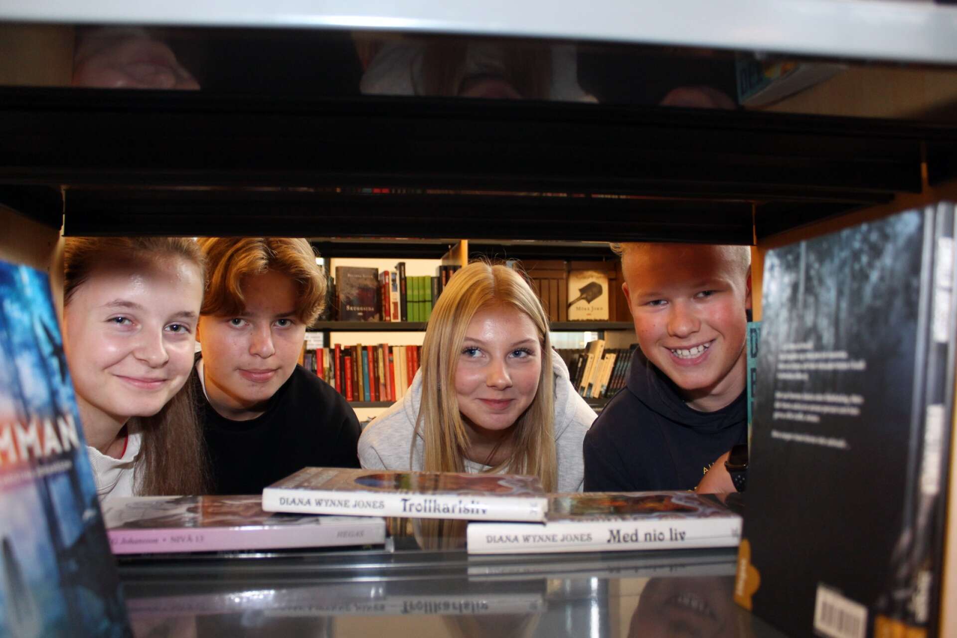 Maja Samueljord, Melvin Weghammar, Lova Bäckman Dahlström och Gustav Skålén i elevrådet på Tegnérskolan tittar fram i en bokhylla på skolans nyinvigda bibliotek. 