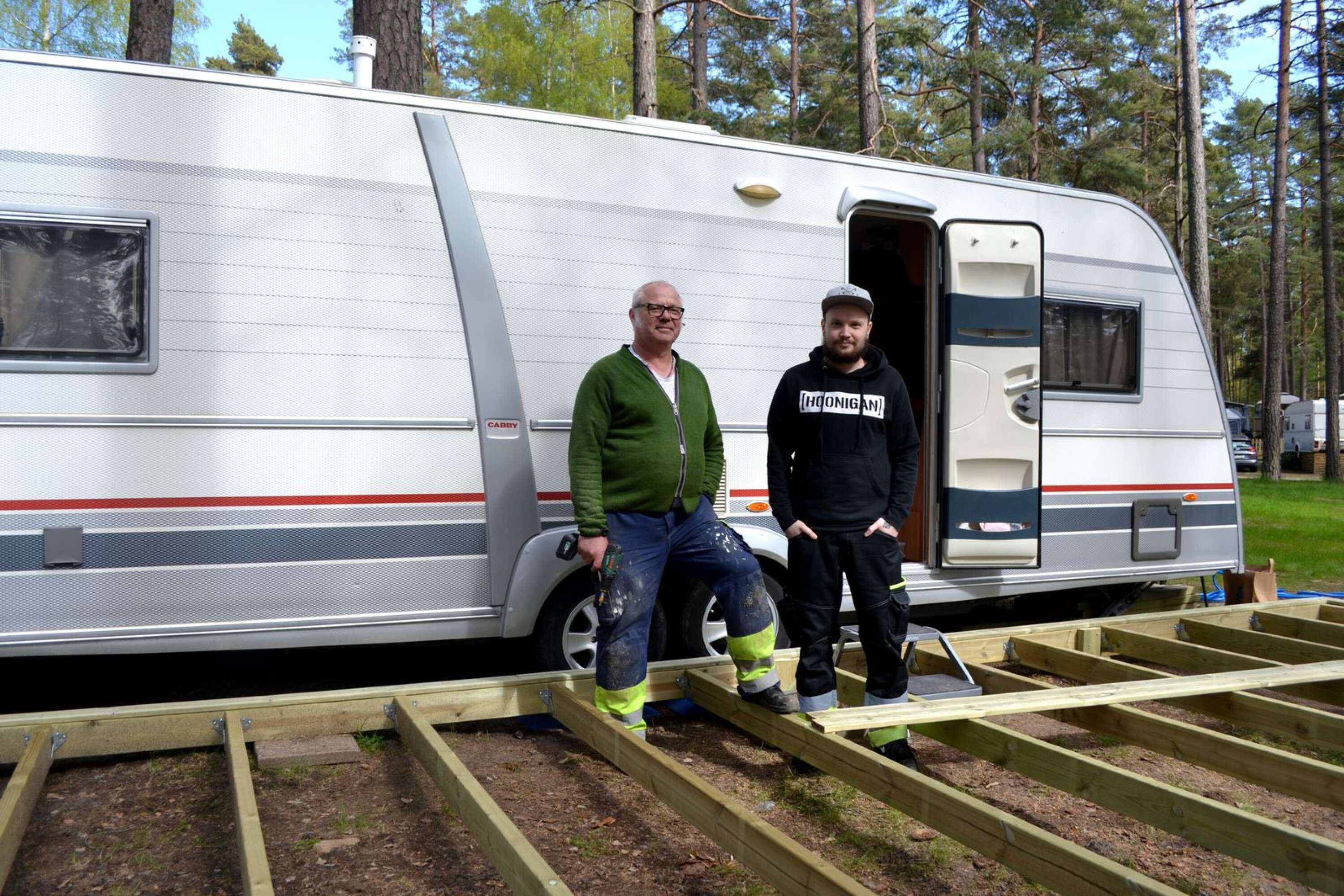 Mikael och Robin Port bygger trädäck utanför husvagnen.