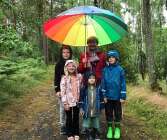 En regnig fredag i mässvik. Barnbarnen Nils, Nora, Loke och Cornelis söker skydd under farmor Ingelas regnbågsparaply.