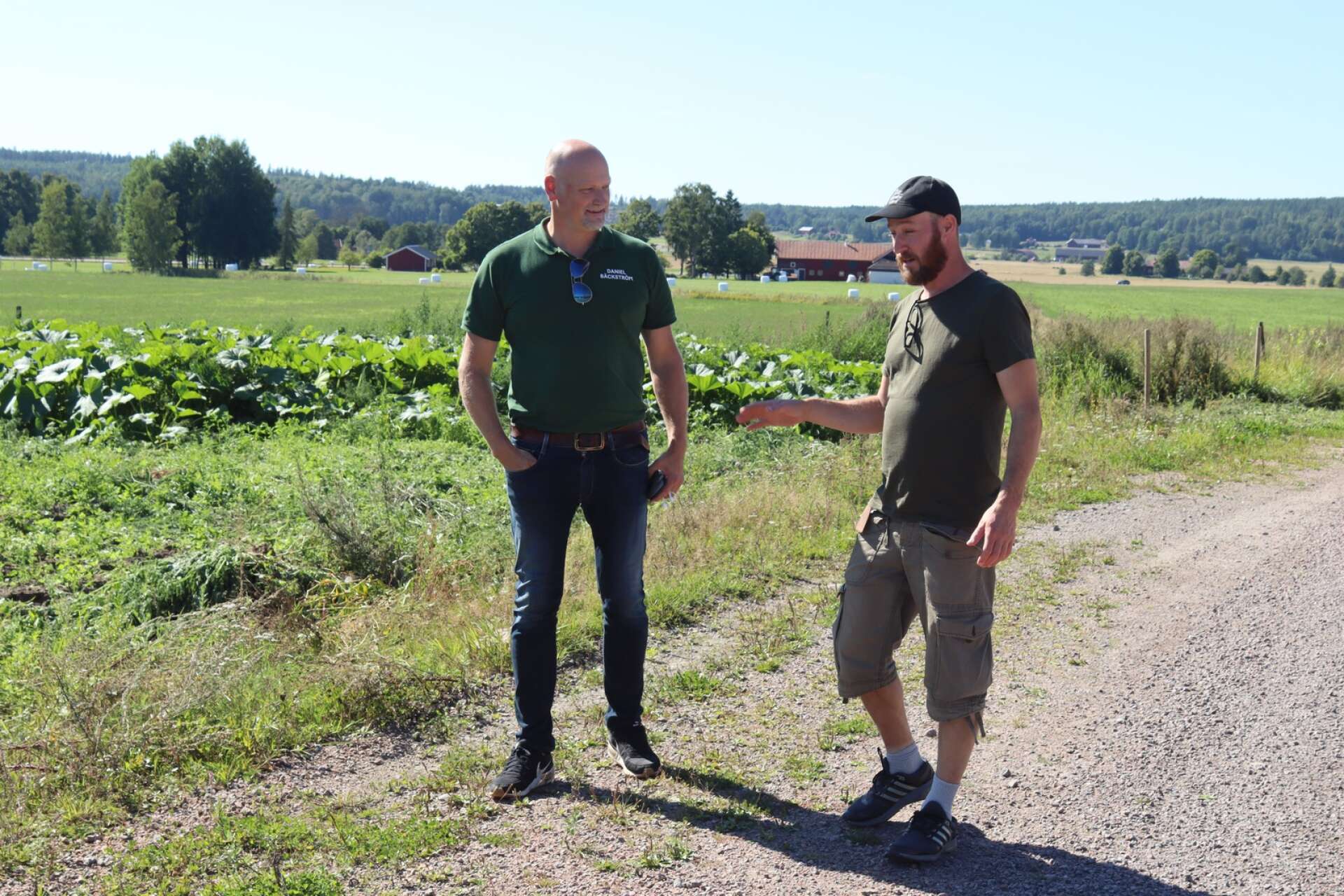 Daniel Bäckström lyssnar när Henrik Herminge berättar om gårdens grönsaksodlingar i bakgrunden.