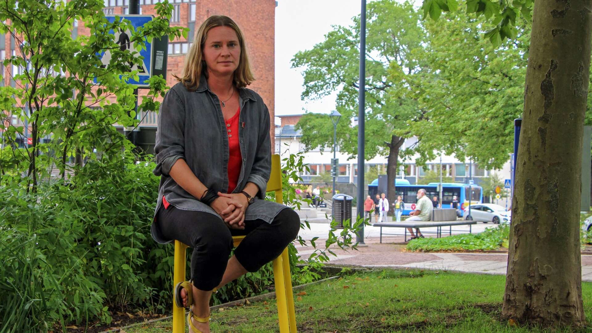 Annika Holmén (V) vill se lägre biljettpriser och kortare arbetsdagar för vårdpersonalen. Hon har valt en fotograferingsplats i det gröna med kollektivtrafik i bakgrunden.