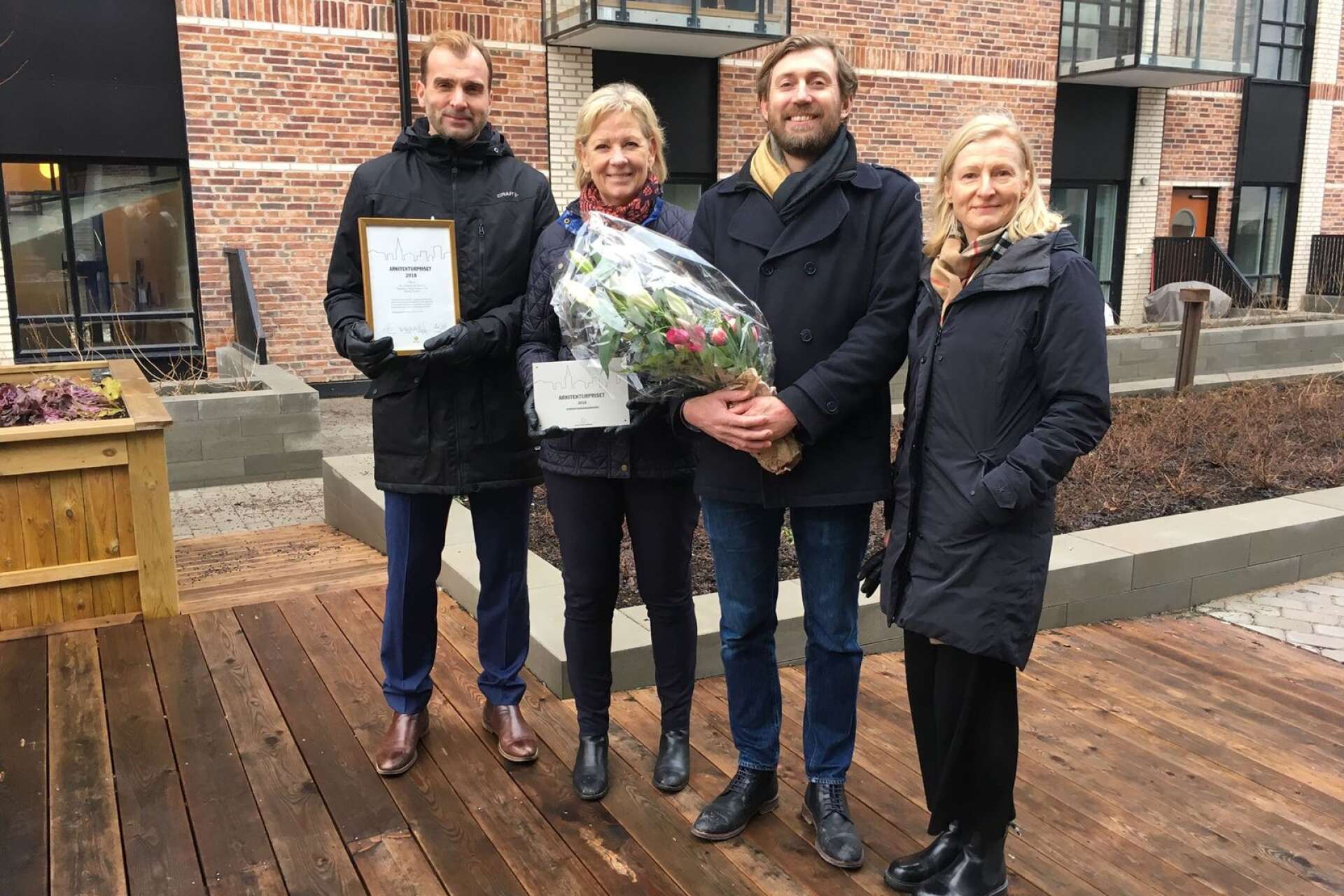 Med det vinnande teglet Red shade i bakgrunden tar byggherren Tomas Rhös och ordförande i BRF Docklands Lotta Hallström emot arkitekturpriset tillsammans med arkitekterna Rémi Mazzenga och Anki Haasma.