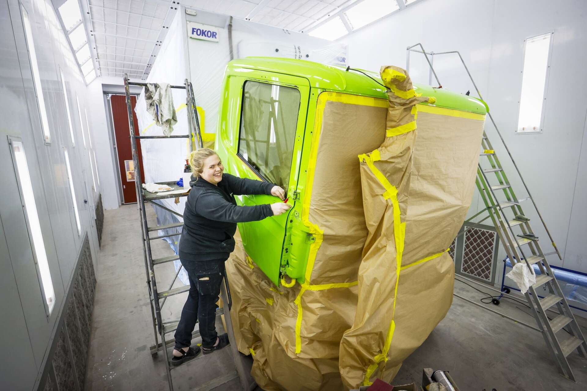 Viktoria Löfgren tejpar och slipar lastbilarna och maskinerna som företaget får in, här en grön truck som ska fräschas upp.