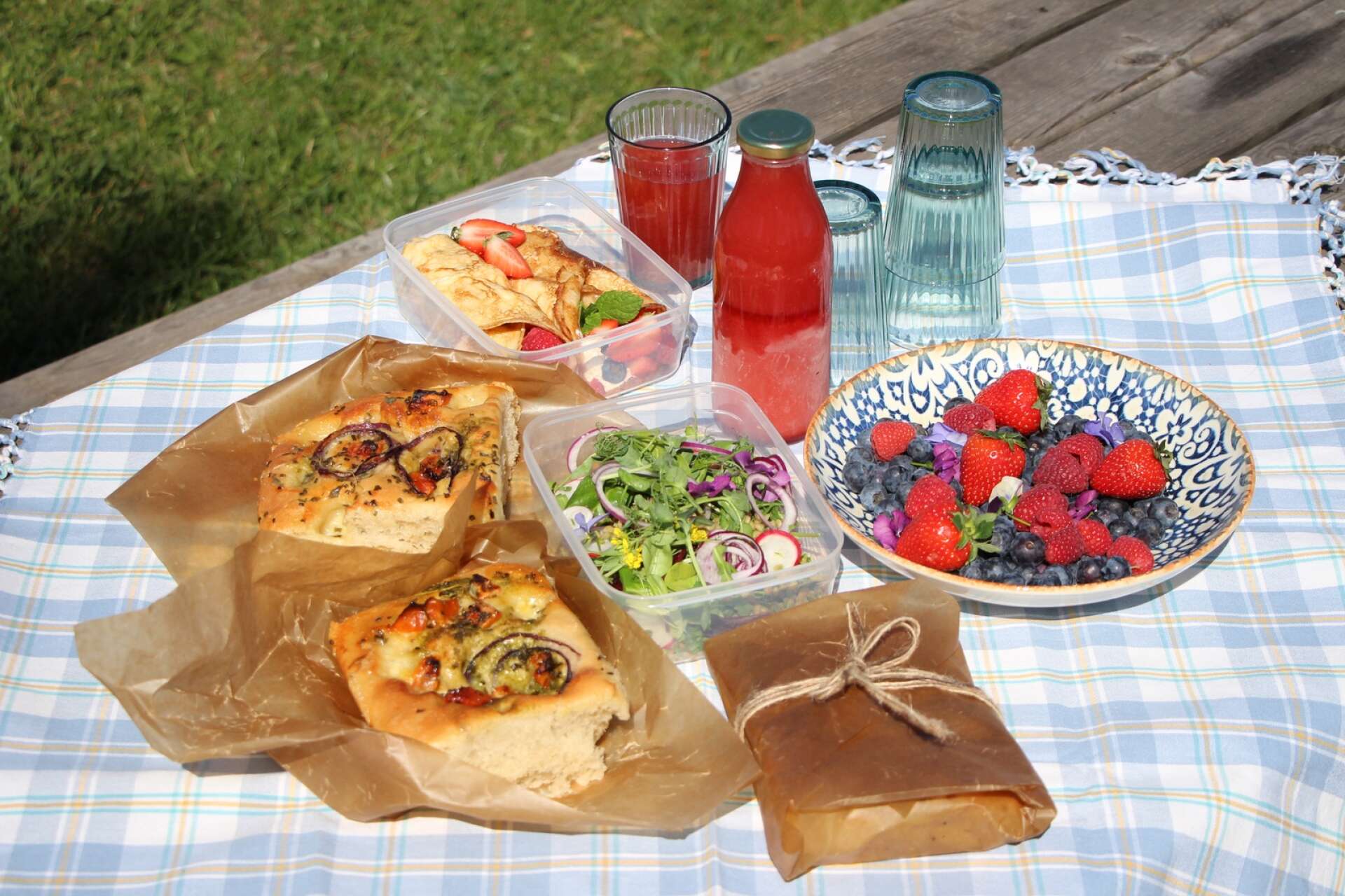 En matig picknick med rätter som räcker till både lunch och mellanmål: fylld focaccia, sallad, och surdegspannkakor med färskost och bär samt kallrörd jordgubbssaft. 