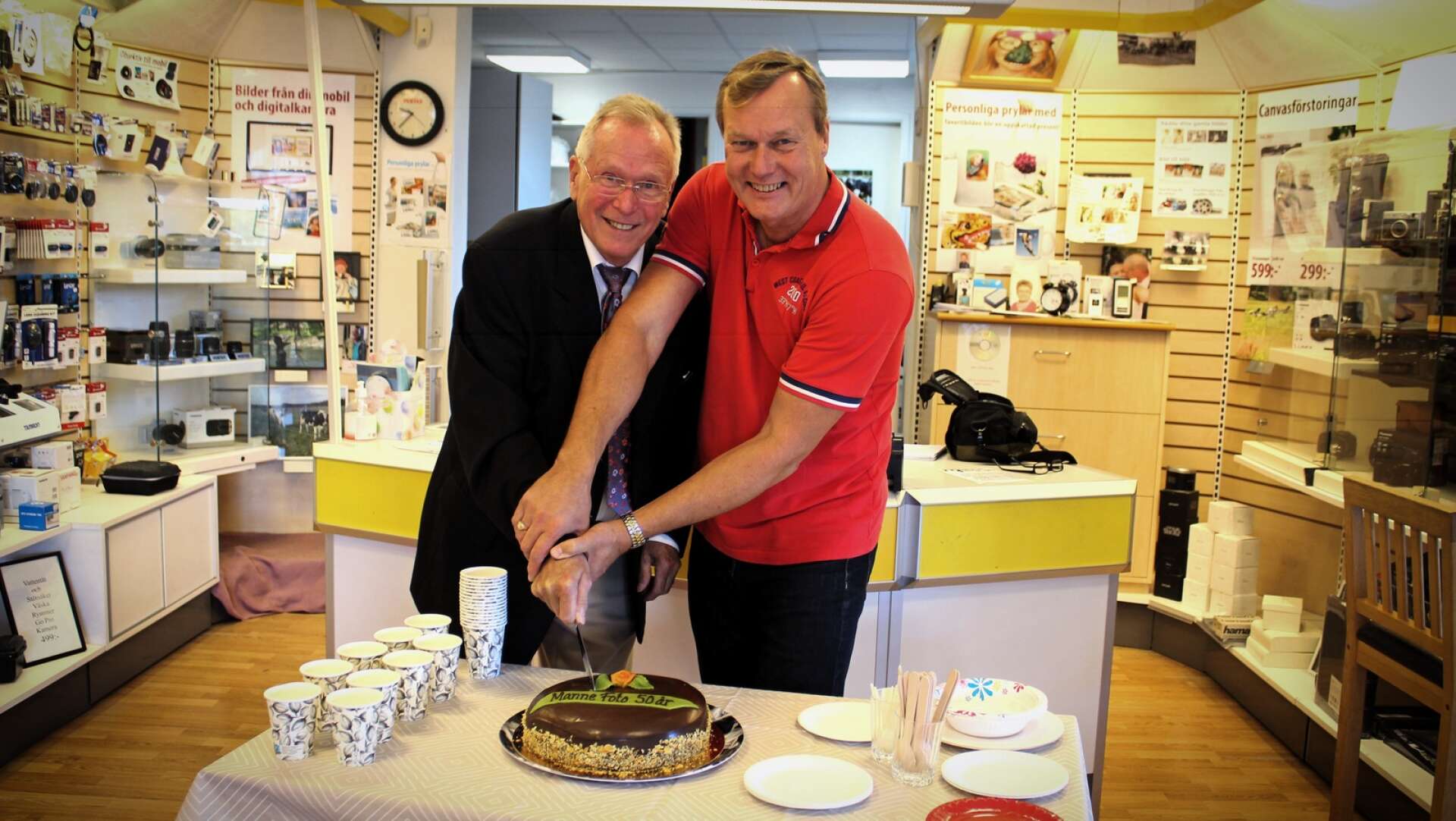 Manne Bergman och Ronny Karlsson hugger in på tårtan på Manne Fotots 50-årsjubileum.