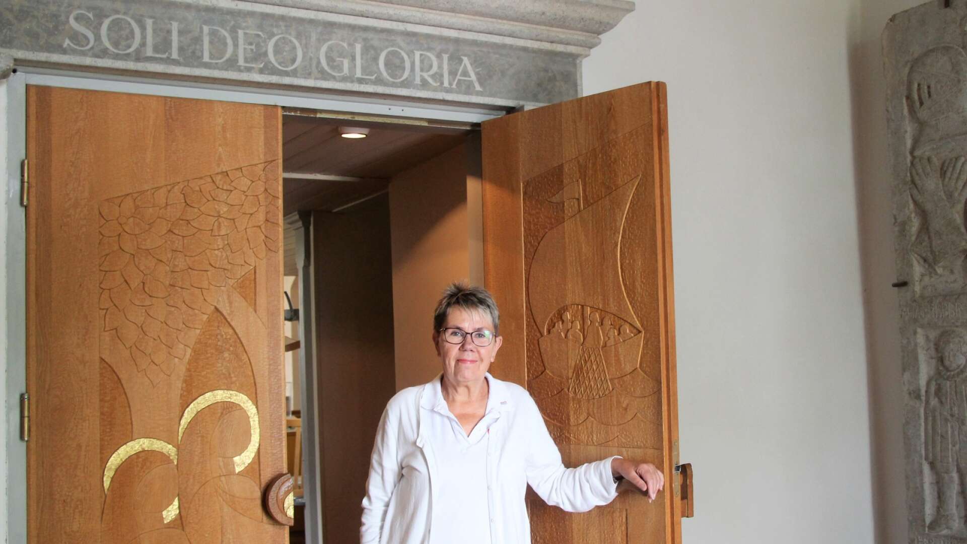 Jane Bäckman är en av de ideella som ser till att Hjälstad kyrka står öppen för besökare i sommartid. ”Soli deo glori” som står över kyrkporten är latin för ”Ära åt Gud allena”.