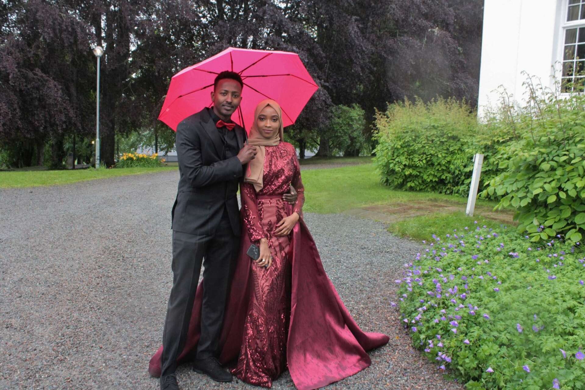 En dam med vinröd klänning som kunnat vara värdig en drottning och en kavaljer med färgmatchande paraply och fluga. Ramla Ahmed och Fuad Hersi gjorde en storstilad entré på gårdsplanen.