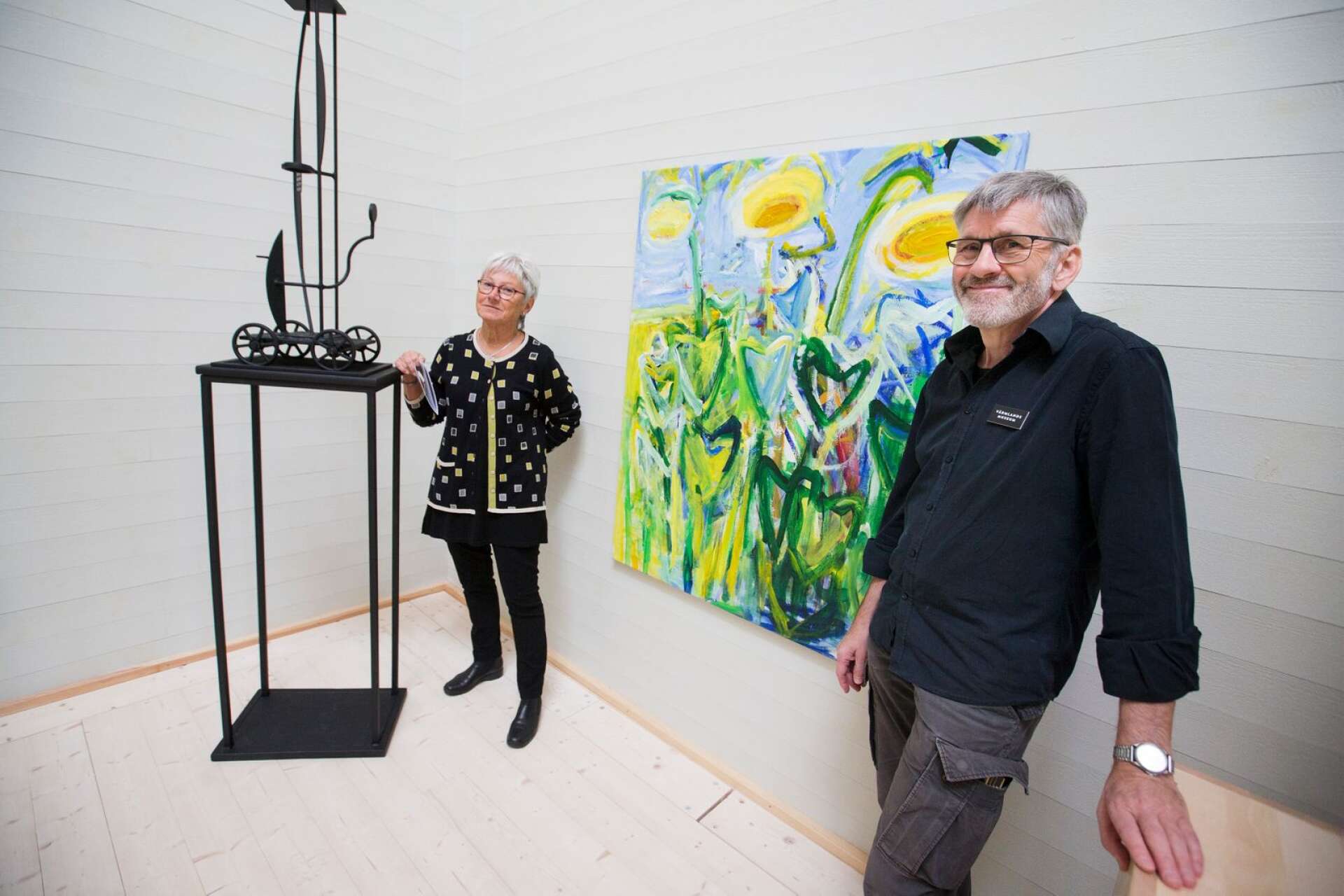 Konstnären Johan Magnusson har hängt årets Höstsalong. Och här står han med konstföreningens Lena Bonnevier vid Gerd Görans blomstermotiv och Nils Johannessons stålskulptur.