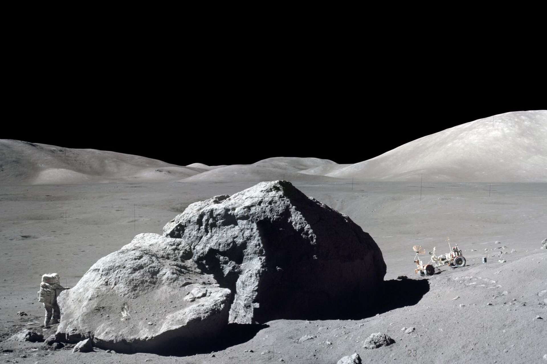 Jack Schmitt vid Tracy&apos;s Rock med Taurus-Littrow-dalen i bakgrunden. Tittar man riktigt noga kan man se månlandaren som en glittrande prick långt borta.