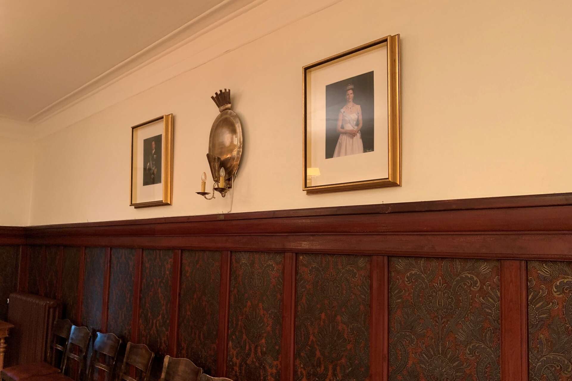 Tavlor av kung XIV Carl Gustaf och Drottning Silvia hänger på kortsidan i matsalen.