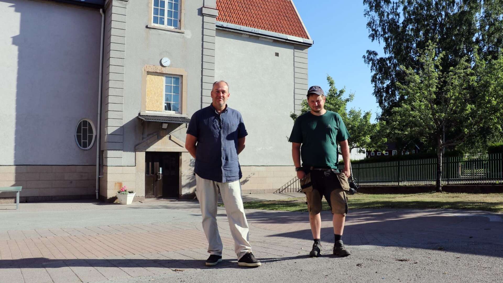 Åmåls Kommunfastigheters vd Magnus Dalsbo och fastighetsskötaren Andreas Dahlgren visar runt på Södra skolans skolgård. Över ena ingången till den grå byggnaden har ett helt fönster krossats.