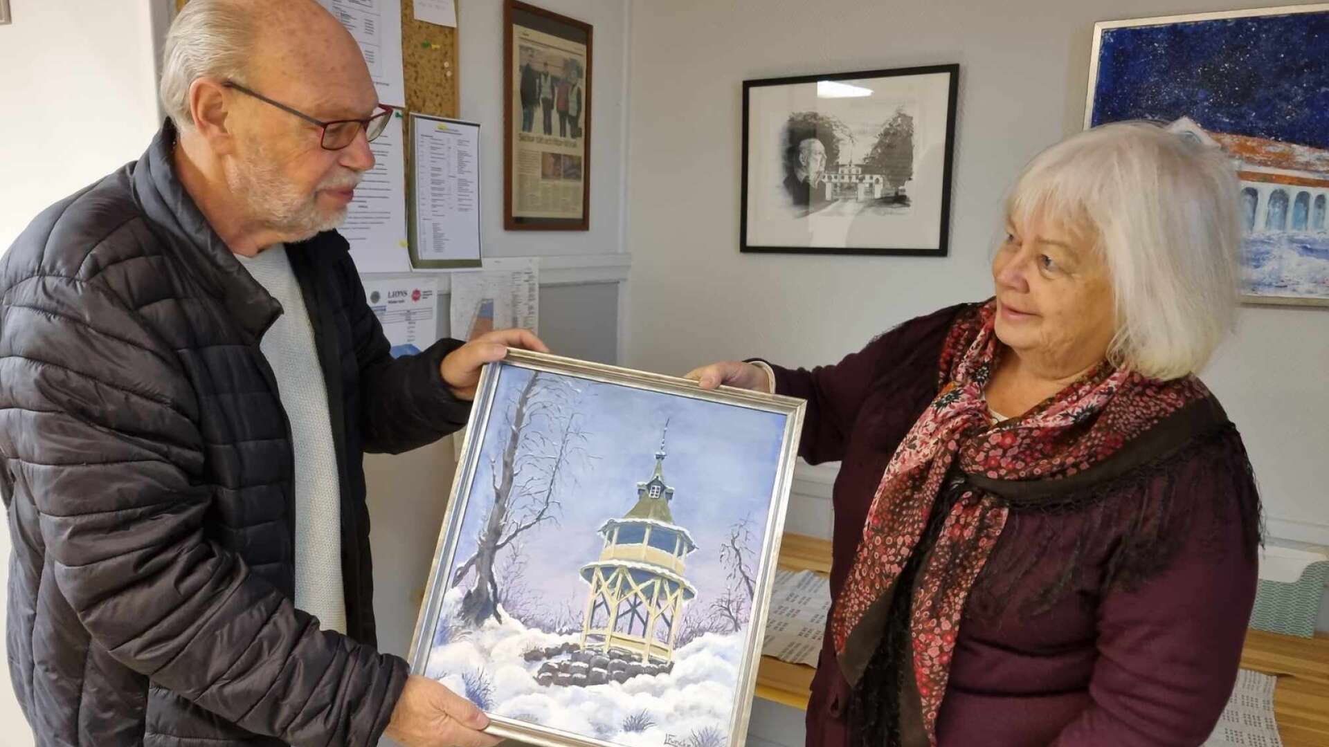 Rolf Karlsson på Lions tar emot årets Jultjugofemman-tavla från konstnären Lena Funcke. Ramen har Glaskedjan skänkt. 