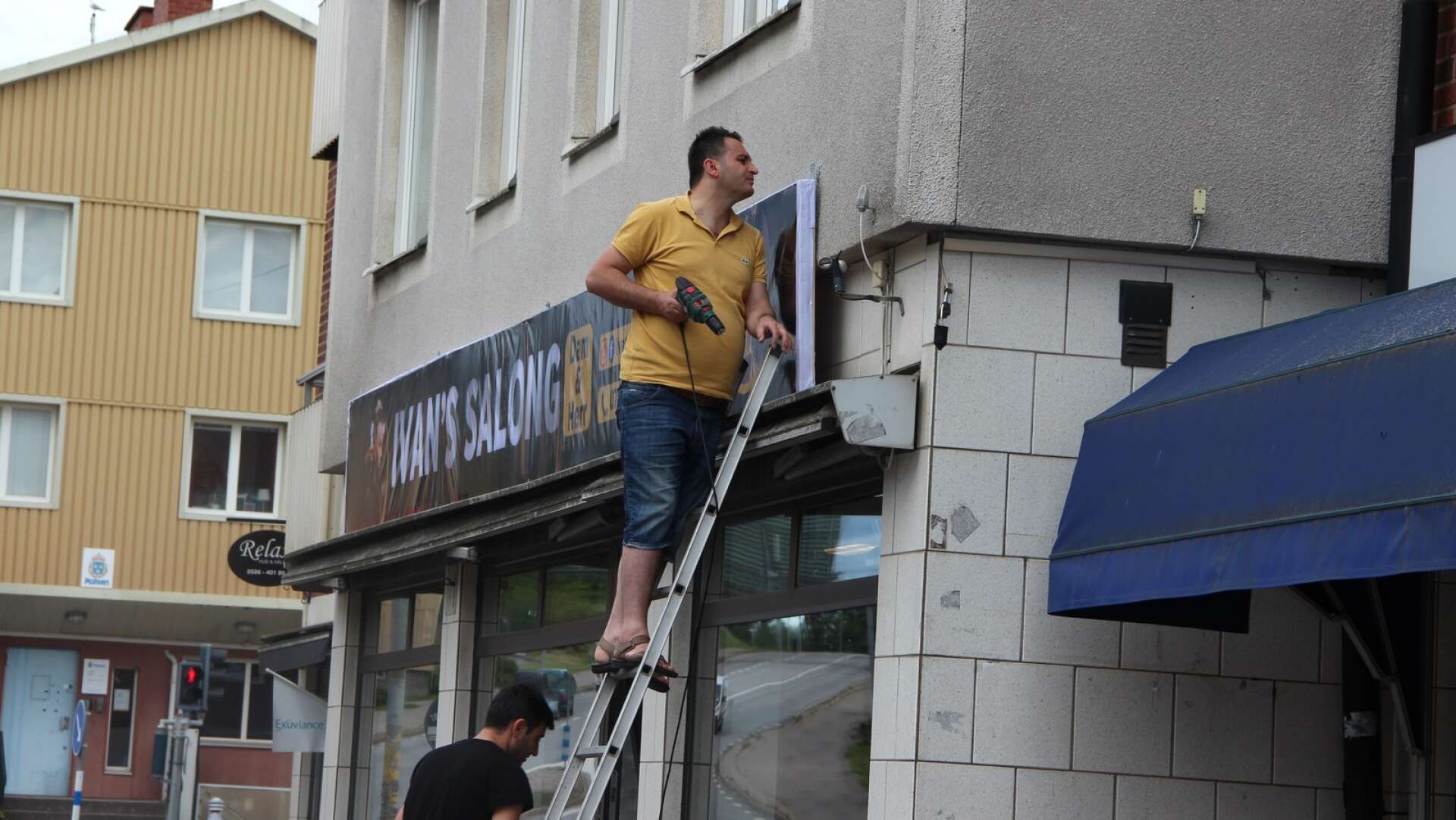 Här skruvar Zuher Ommar upp skylten till den nya Ivan&apos;s Salong &amp; Barbershop i Degerfors.