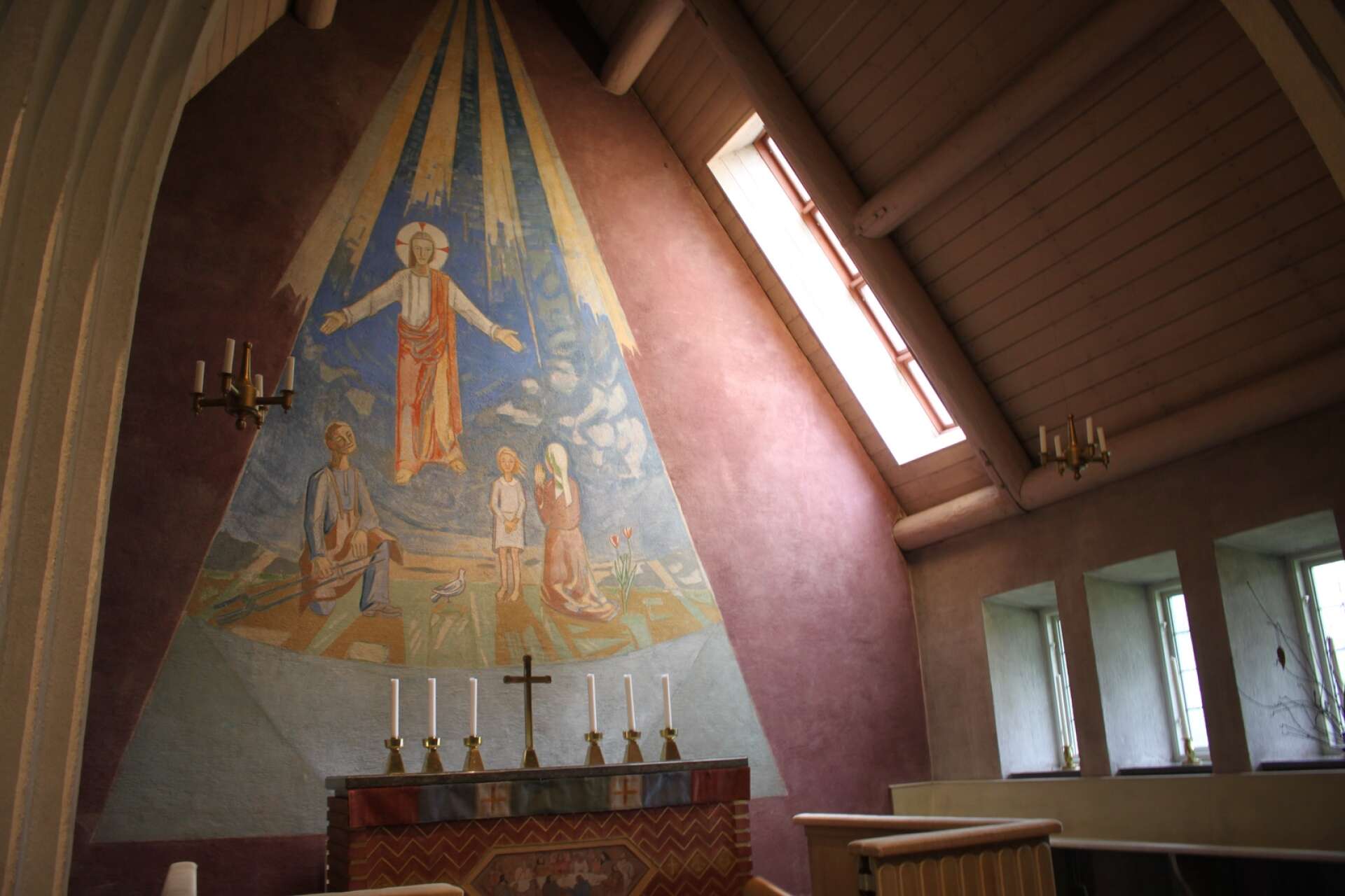 Sven Rapp har målat den ståtliga altarmuralmålningen. Sneda takfönster med snillrik placeringar gör artificiell belysning överflödig vid högmässa.