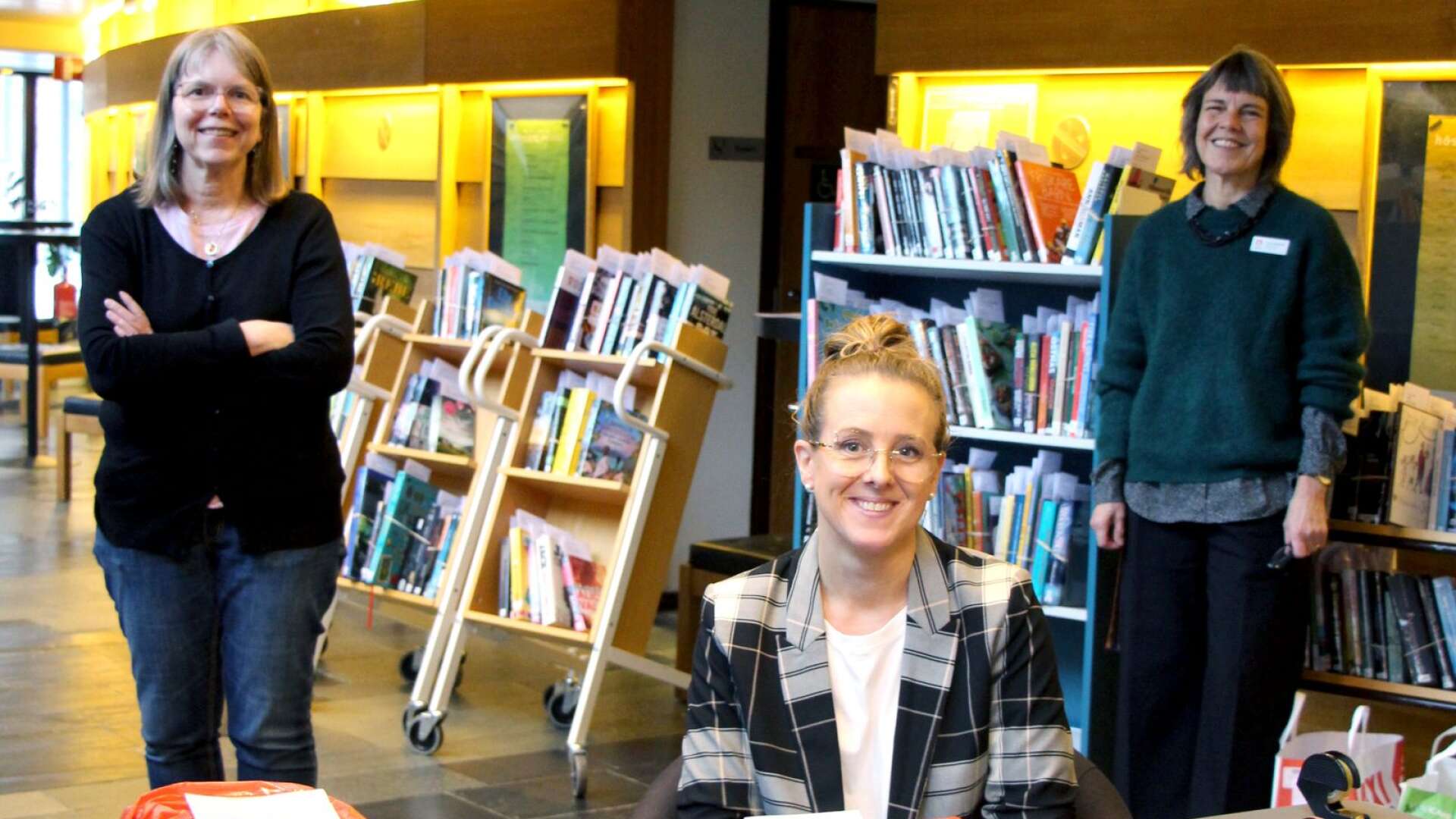 Bibliotekarie Lena Wellman, biblioteksassistent Carolina Tholin, och bibliotekschef Anna Gullstrand i teaterfoajén där utlämningen av böcker sker. Den som har ringt och aviserat sin ankomst får sin beställning färdigpackad i en röd påse.