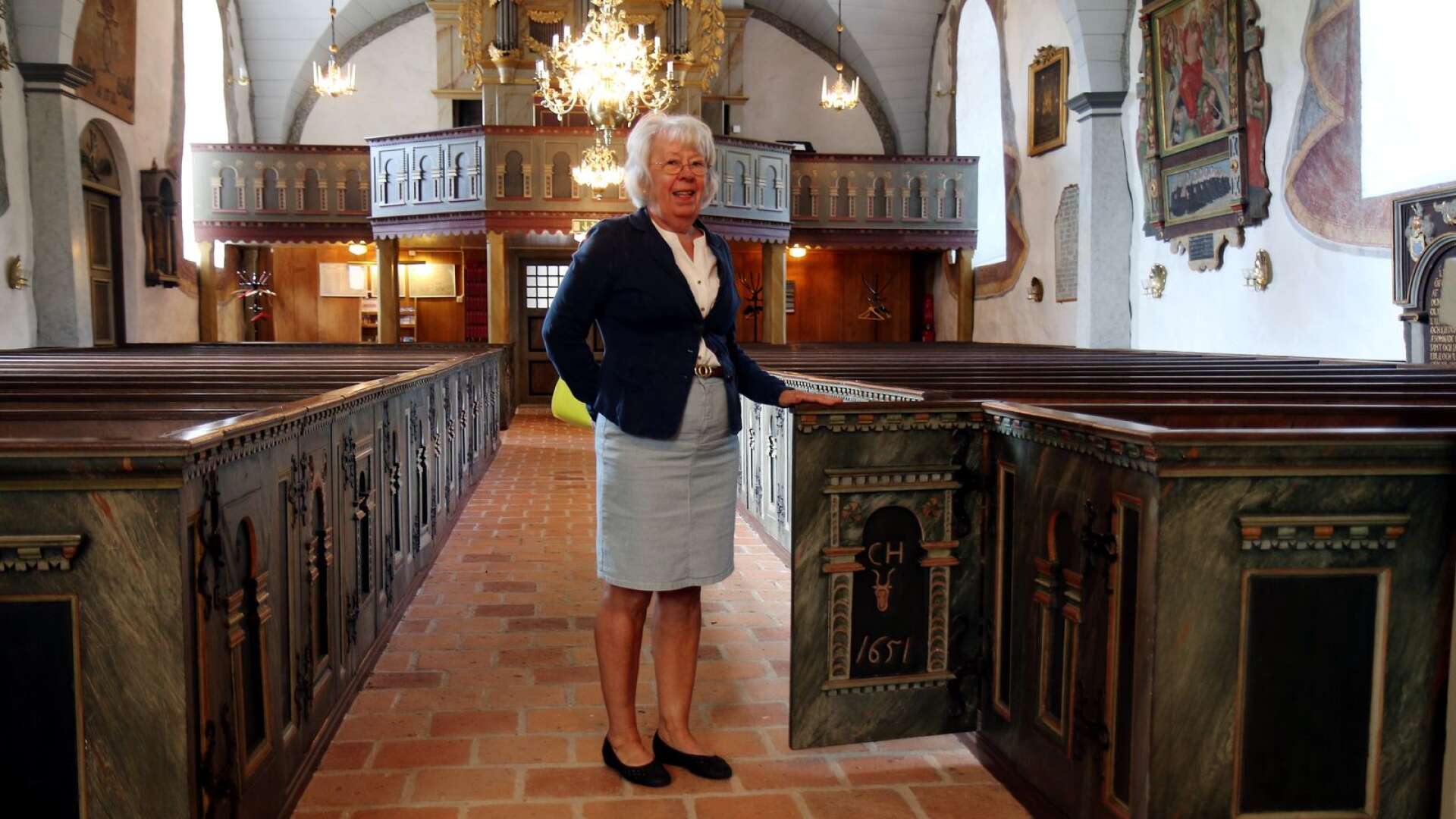 Eva Johansson visar upp bänkdörrarna med familjen Hårds vapen på i Norra Fågelås kyrka.