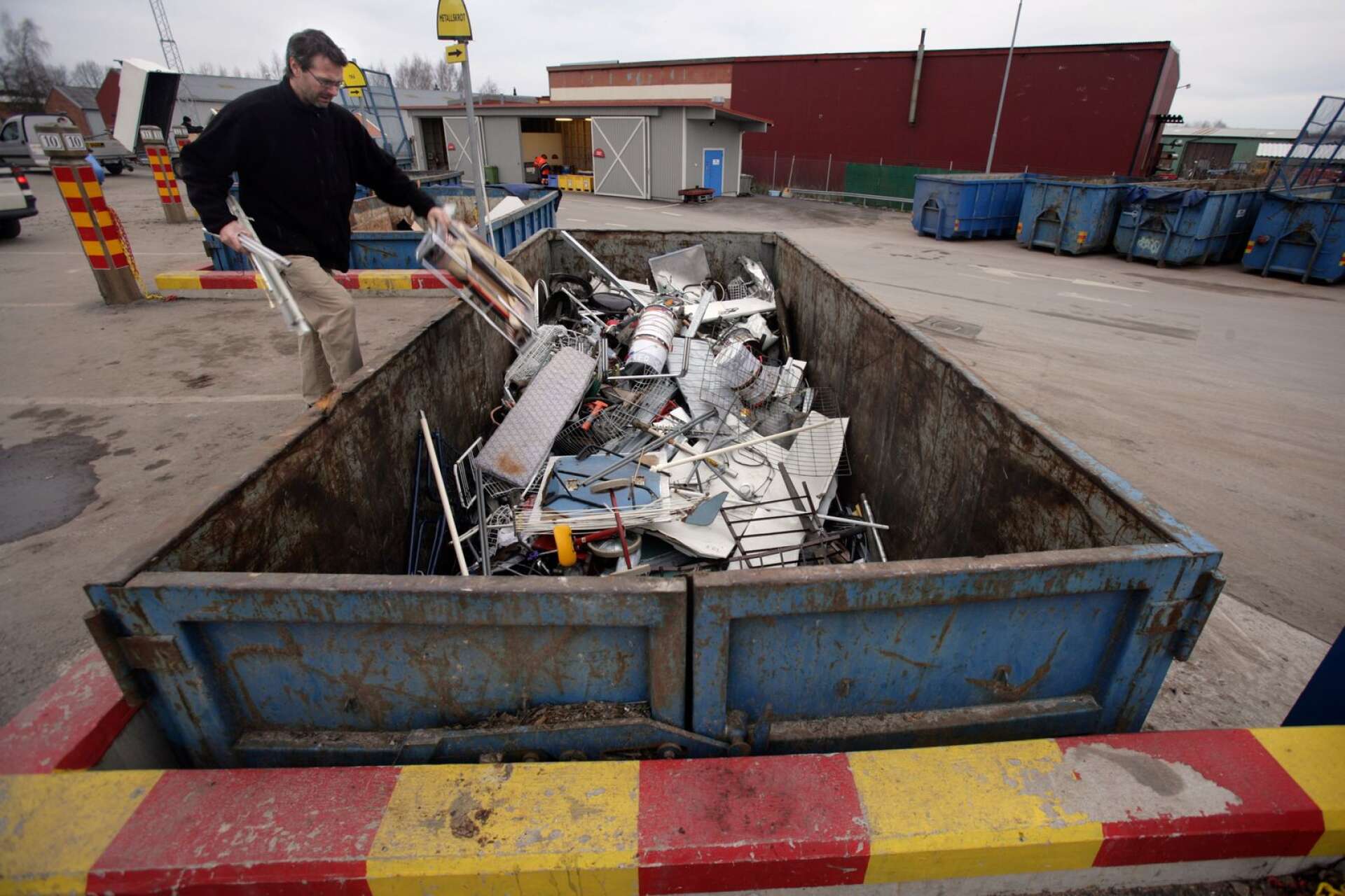 En man slänger metallskrot i en container på en återvinningscentral. Genrebild.