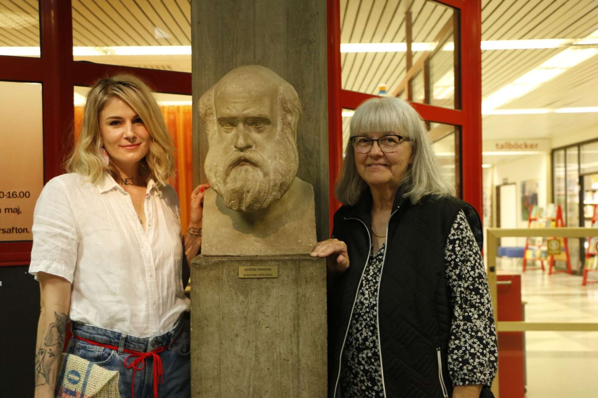 Marthe Hem och Berith Sande vid en skulptur av Gustaf Fröding på Karlstads stadsbibliotek. 