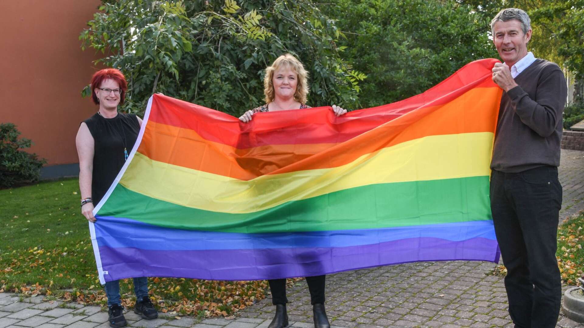Therése Göransson och Karin Arvidsson lämnar över regnbågsflaggan till kommunchefen Per-Ola Arnling Hedberg.