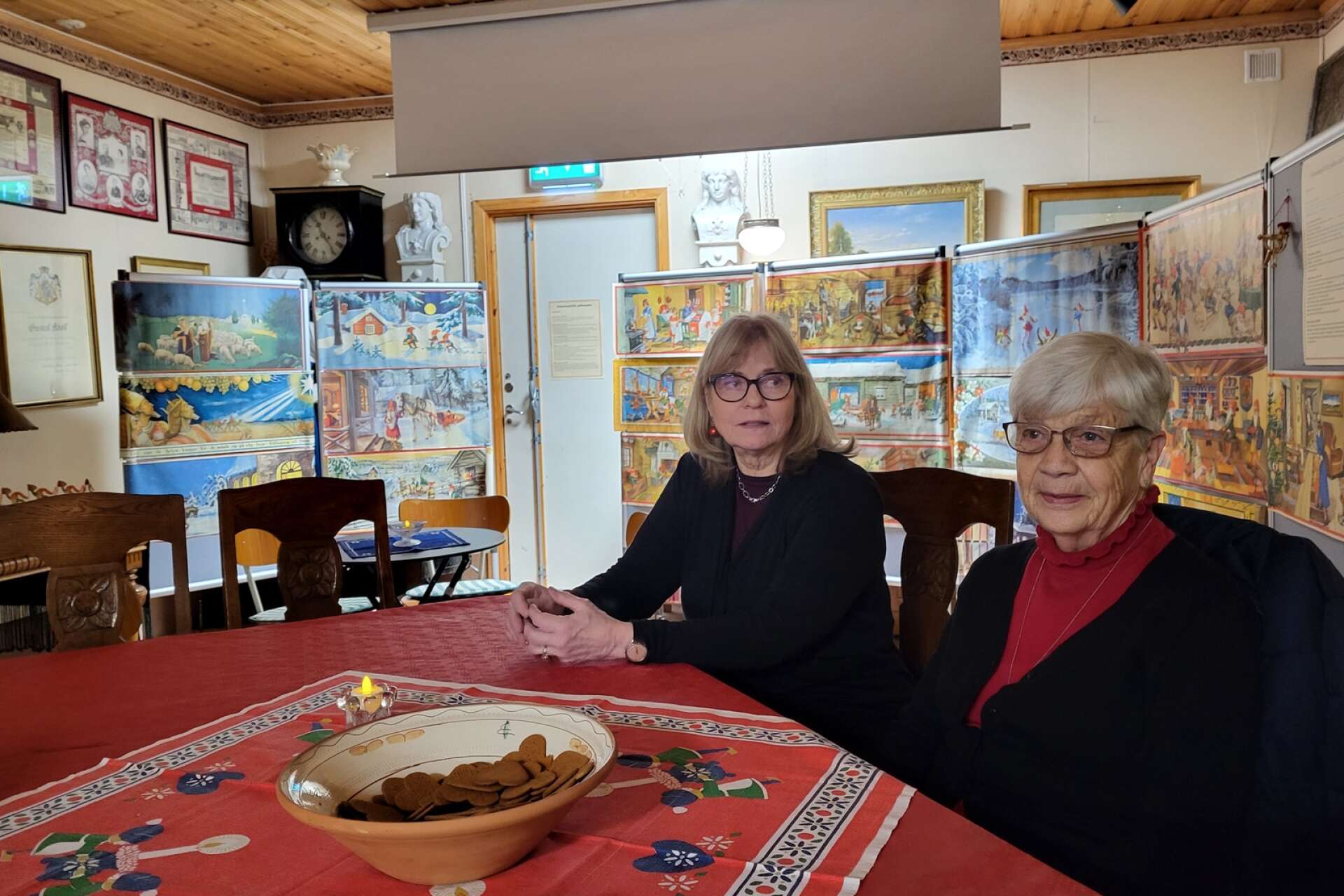 Hembygdsföreningens Margareta Nilars och museibesökaren Asta Andersson har slagit sig ner framför utställningen av klassiska julbonader.