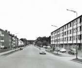 I det då nybyggda huset till höger på bilden öppnades 1 november 1960 livsmedelsbutiken Obe Livs. Närmast kameran ses Cete Möbler. Vallen till vänster hade byggts några år tidigare. Vänstertrafik var det fortfarande.  