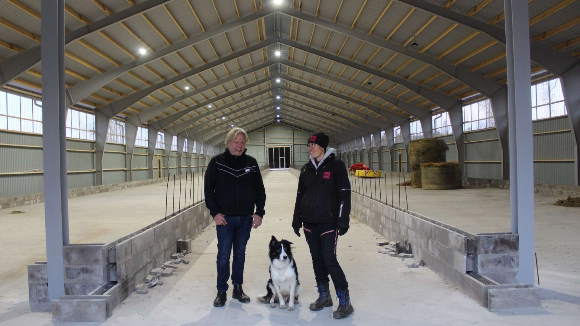 Ett nytt fårhus håller på att ta form på Öxnevåls gård i Kila. På bilden Lars Pettersson, Keiko Schönberg och hunden Sam.