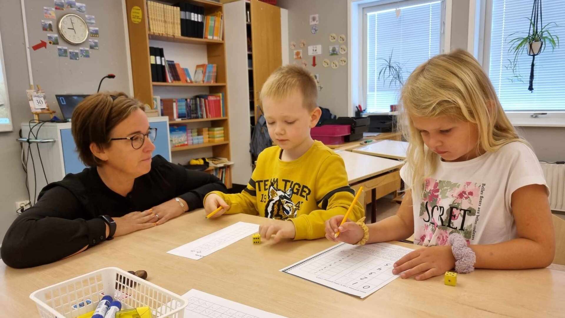 Läraren Lollo Lindberg med Oscar och Astrid. Det är mattelektion för ettorna och med en tärning ska de leta ”femkompisar”. 