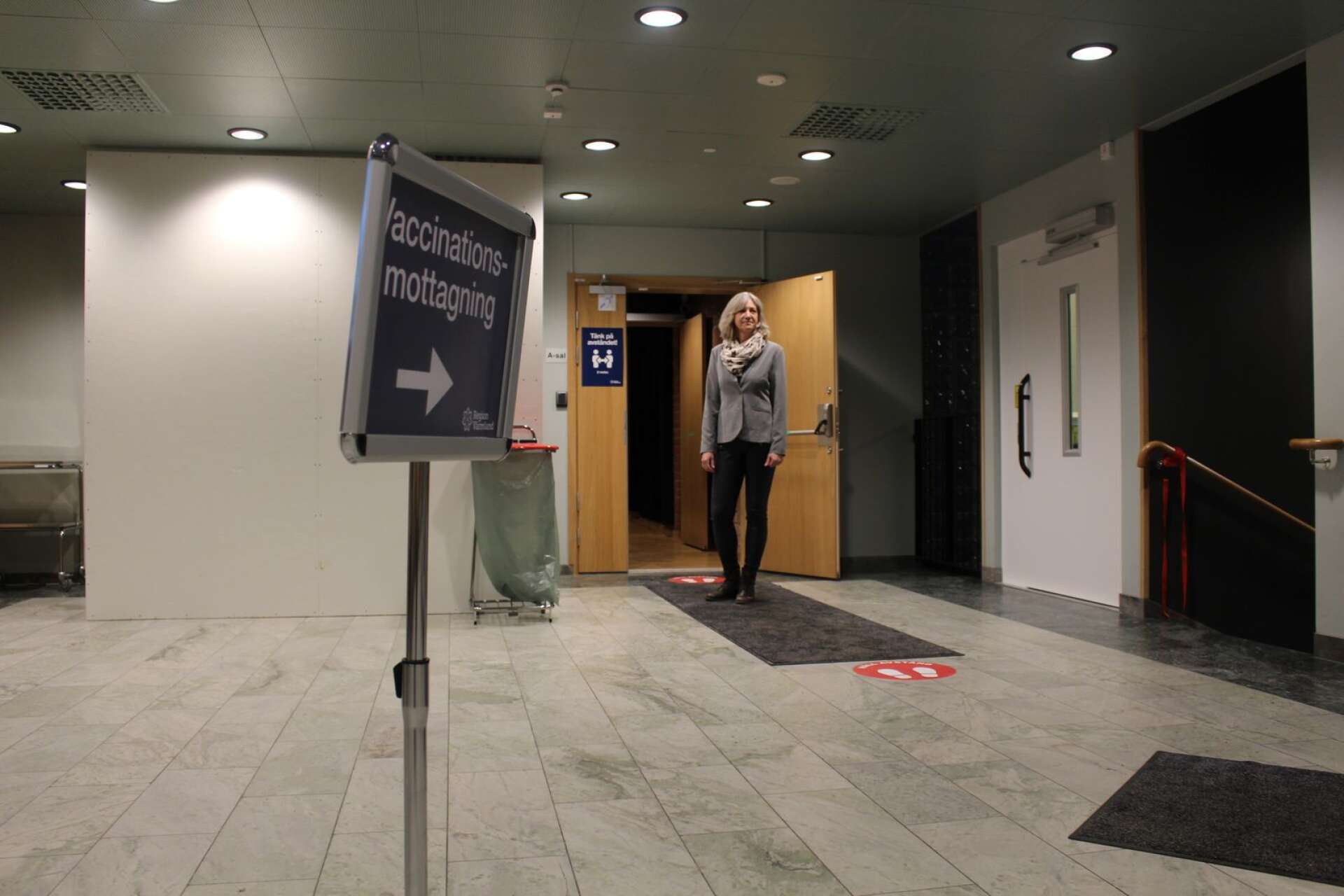 De röda markeringarna på golvet visar hur man ska stå på två meters avstånd när man väntar på att slussas in till ett av vaccinationsbåsen. På bilden syns Kristina Högberg, chefssekreterare på Region Värmland.