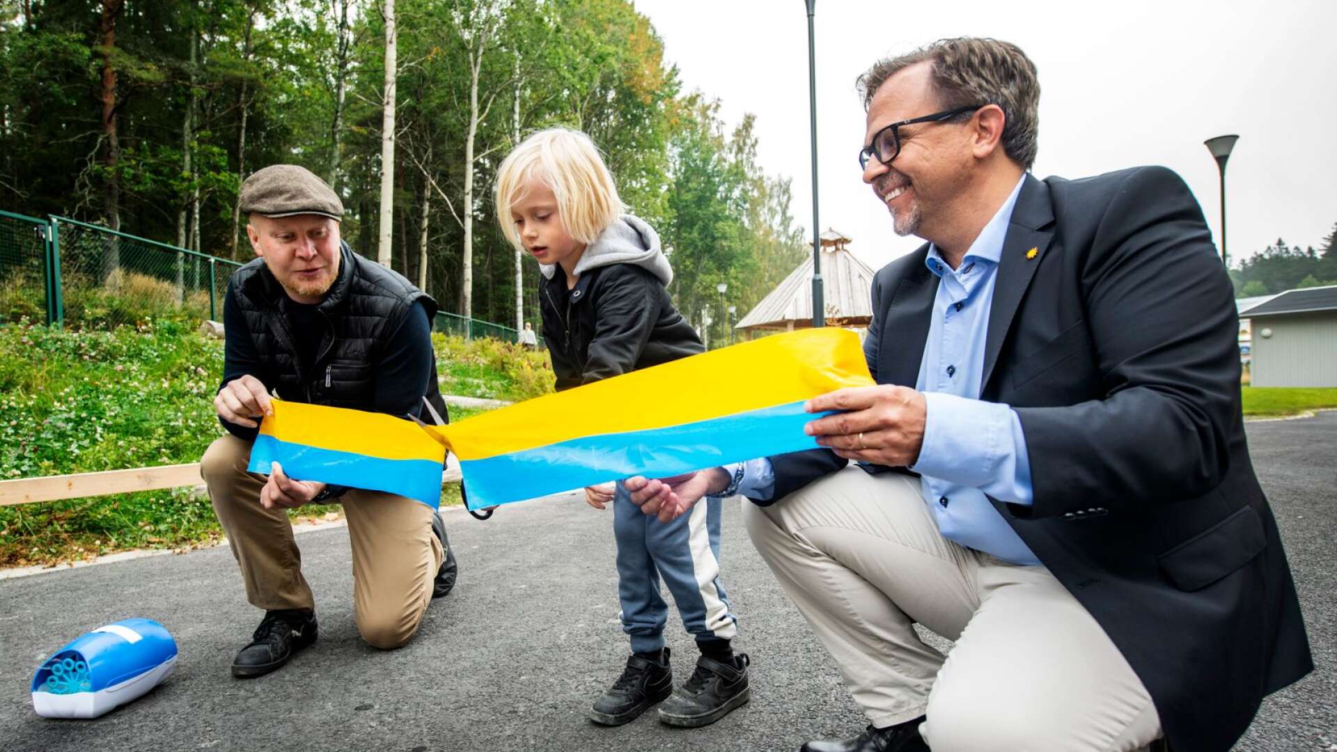 Gillis Träff klipper invigningsbandet som Henrik Lander, ordförande i teknik och fastighetsnämnden (C) och Niklas  Wikström (L), ordförande i barn- och ungdomsnämnden håller upp.