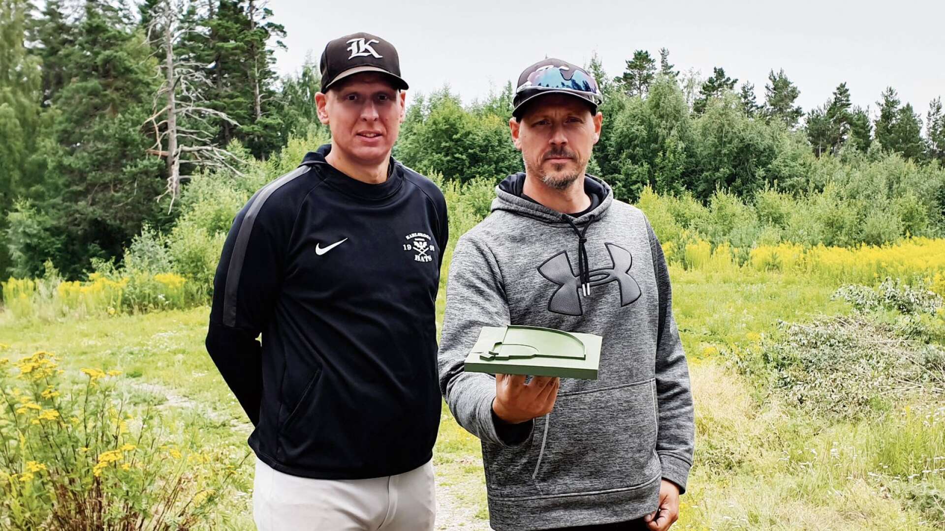 Karlskoga Bats Olle Öijen och Daniel Lindkvist, med en modell över hur nya planen kan se ut, vid området där den nya planen kan anläggas.