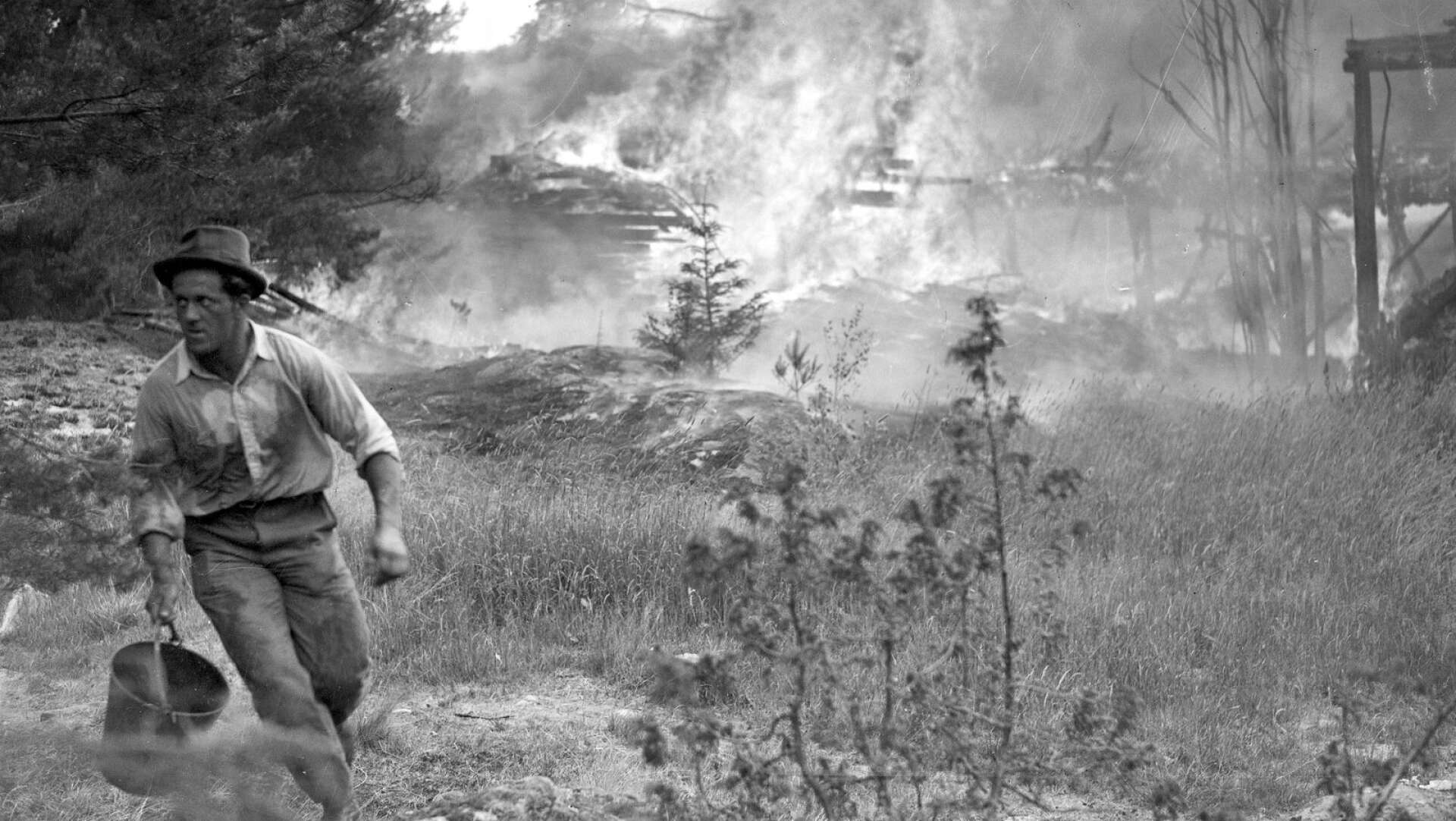 En man springer med en hink för att hämta vatten när elden härjar ekonomibyggnaderna på Trangärdstorps gård den 15 juli 1941. Flera byggnader på gården slukades av eldens lågor. 35 år senare brinner även herrgården.