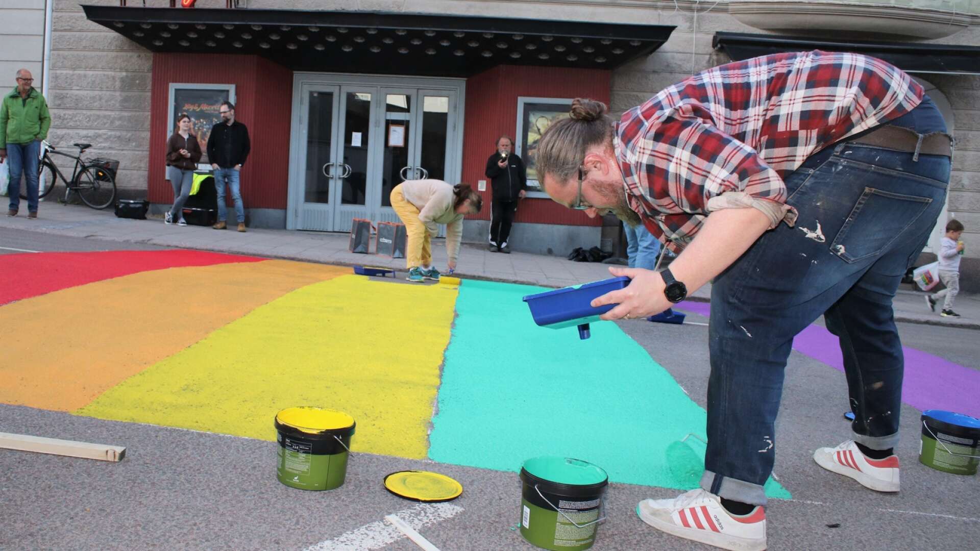 Peter Olsson (V) lägger sista strykningarna på den gröna färgen i den stora Prideflaggan utanför Sagabiografen. 