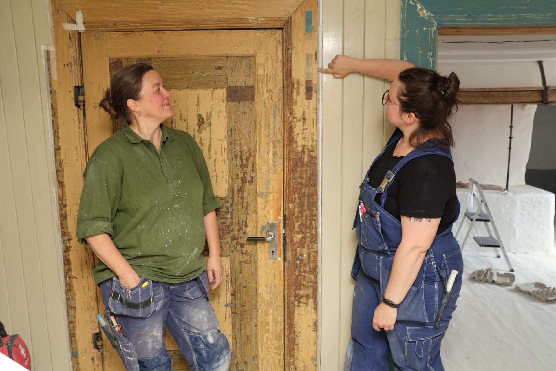 Kulturmålarna Susanne Lundmark och Olivia de Jong, som här visar en av de färgtrappor som de har skrapat fram på en dörr.