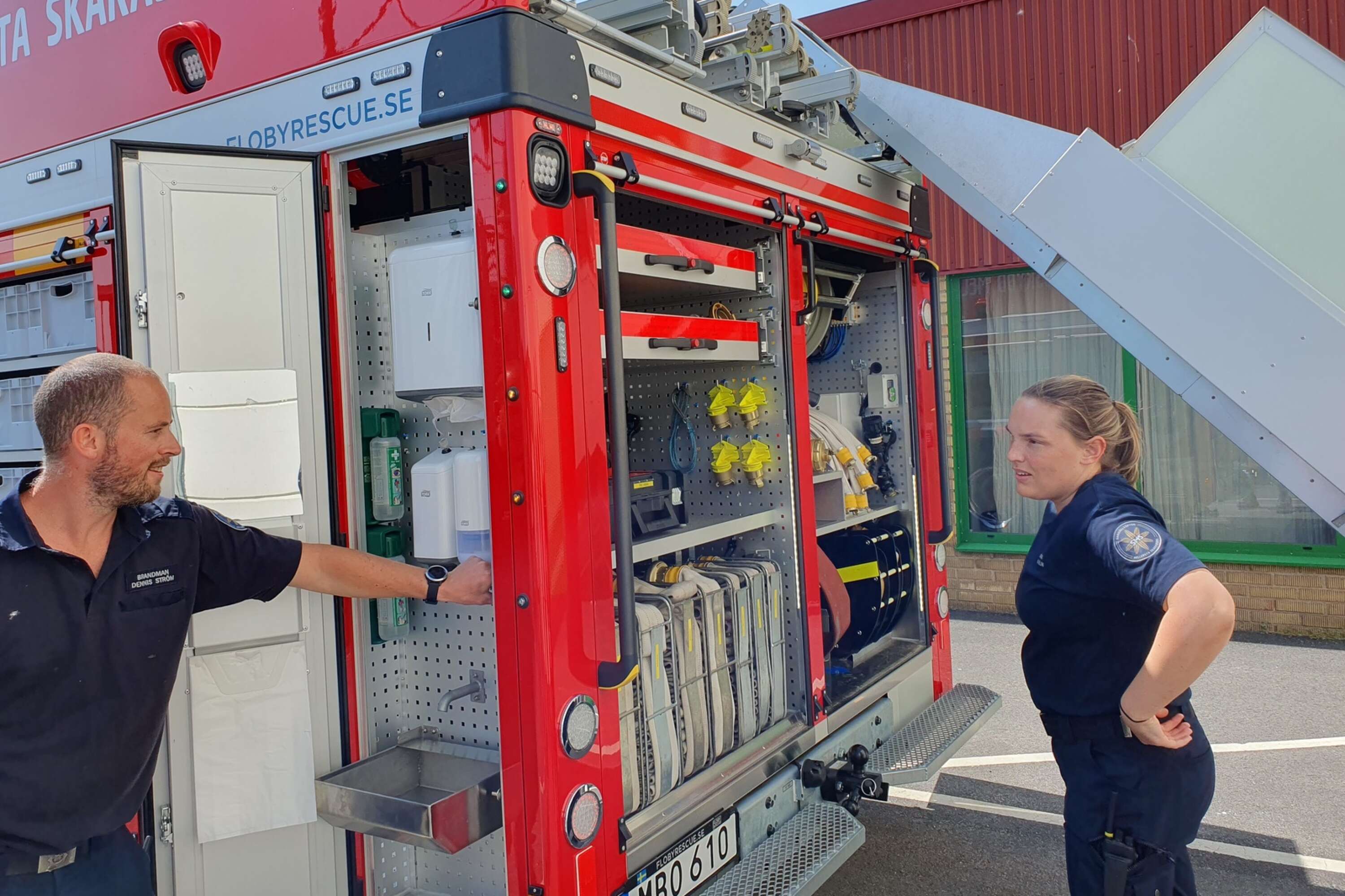 Brandmännem Dennis Ström och Malin Molin vid en ny grej, ”tvättskåpet” där brandmännen kan tvätta av sig vid bilen efter avslutat uppdrag.