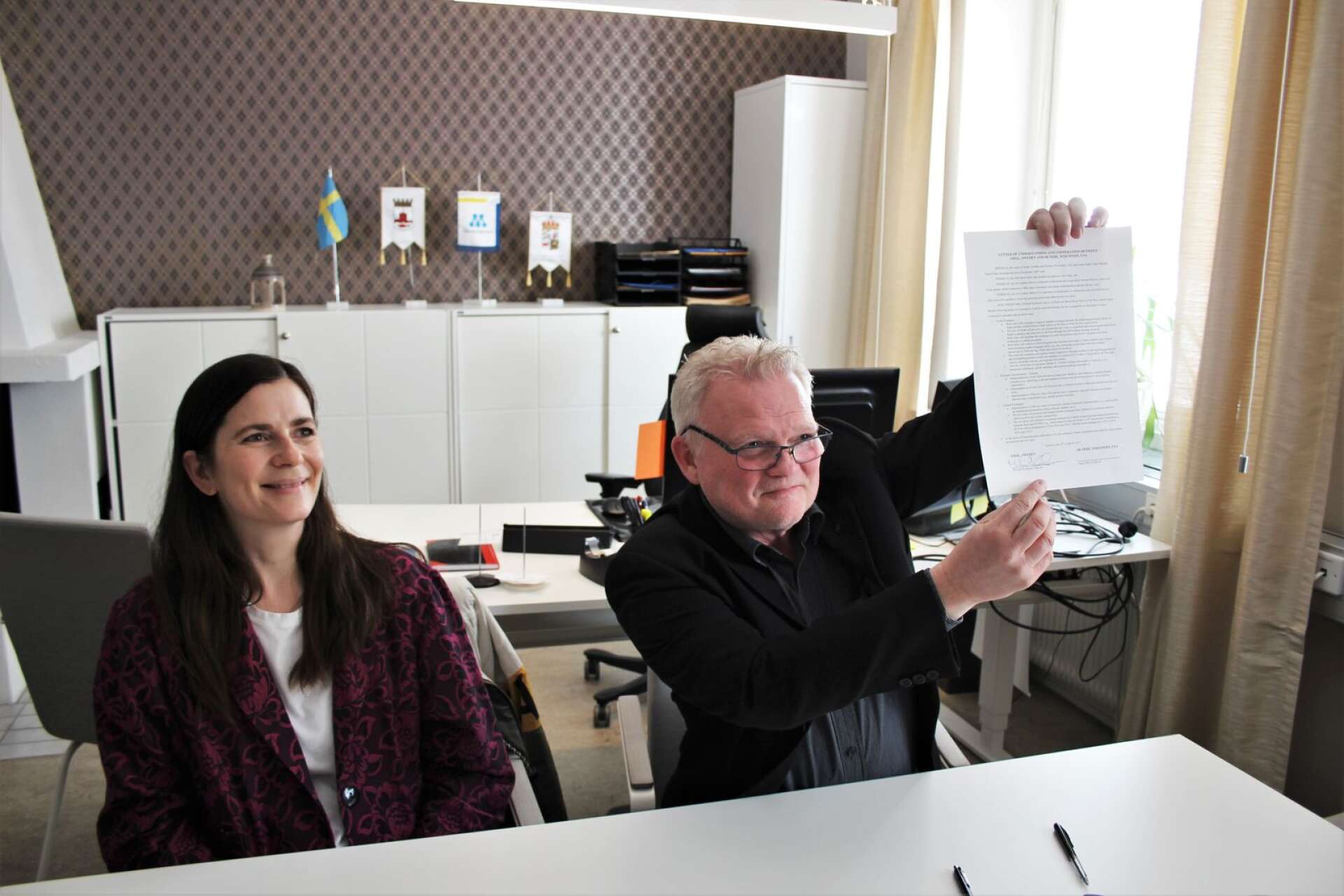 Michael Karlsson håller upp det nyundertecknade avtalet. Bredvid sitter Kristin Björk, kommunens internationelle strateg.