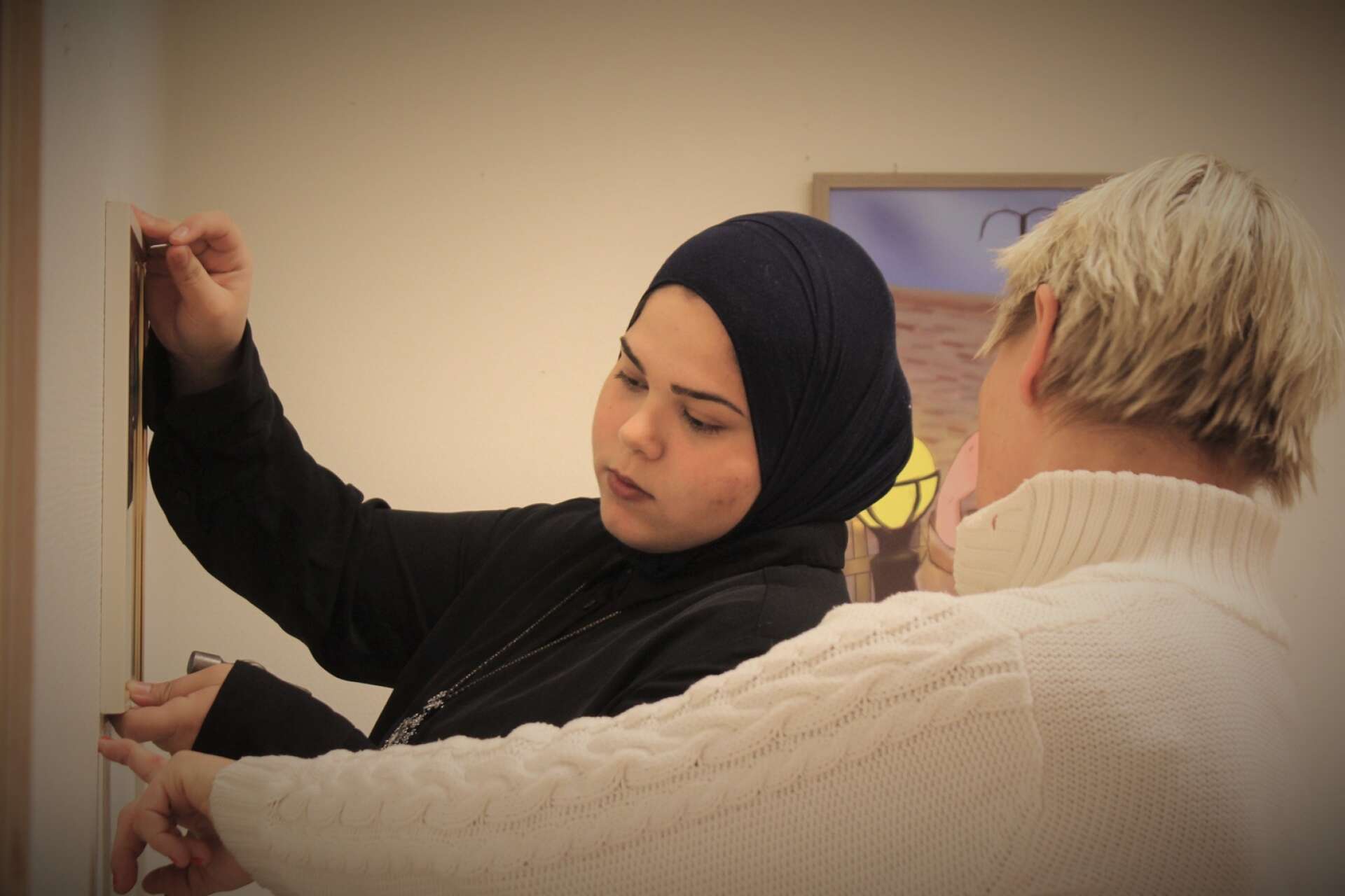 Maya Alfateh får hjälp av kultursekreterare Sanna Seppänen att få tavlorna på rätt plats.