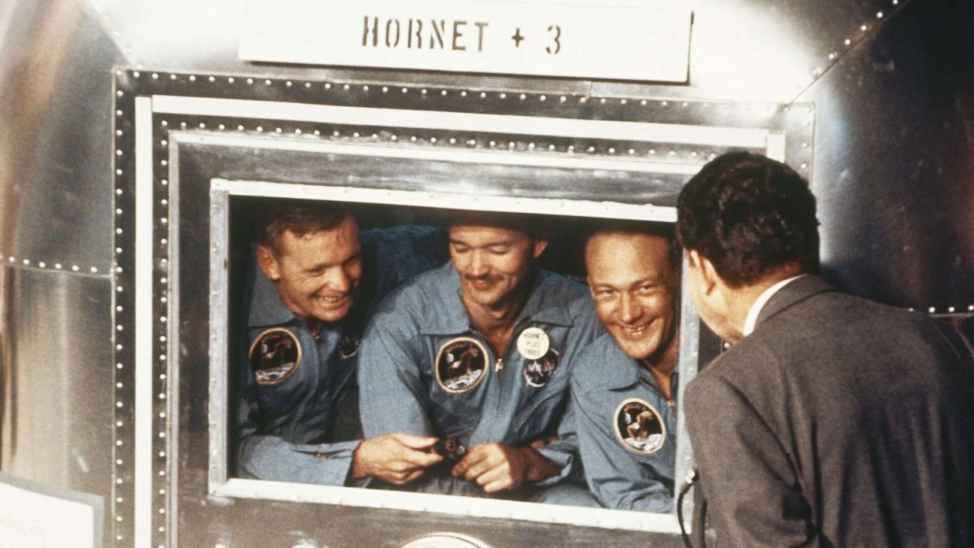 Apollo 11:s besättning tillbaka på Jorden. Där får de – genom glasrutor – hälsa på dåvarande USA-presidenten Richard Nixon.