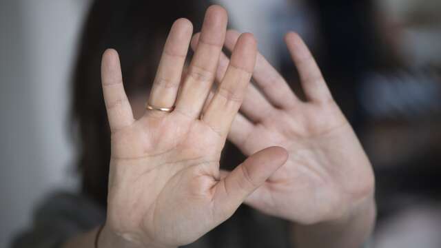 En kvinna sätter upp sina händer för att skydda sig, värjer sig. Mäns våld mot kvinnor, genrebild. Våld i hemmet.