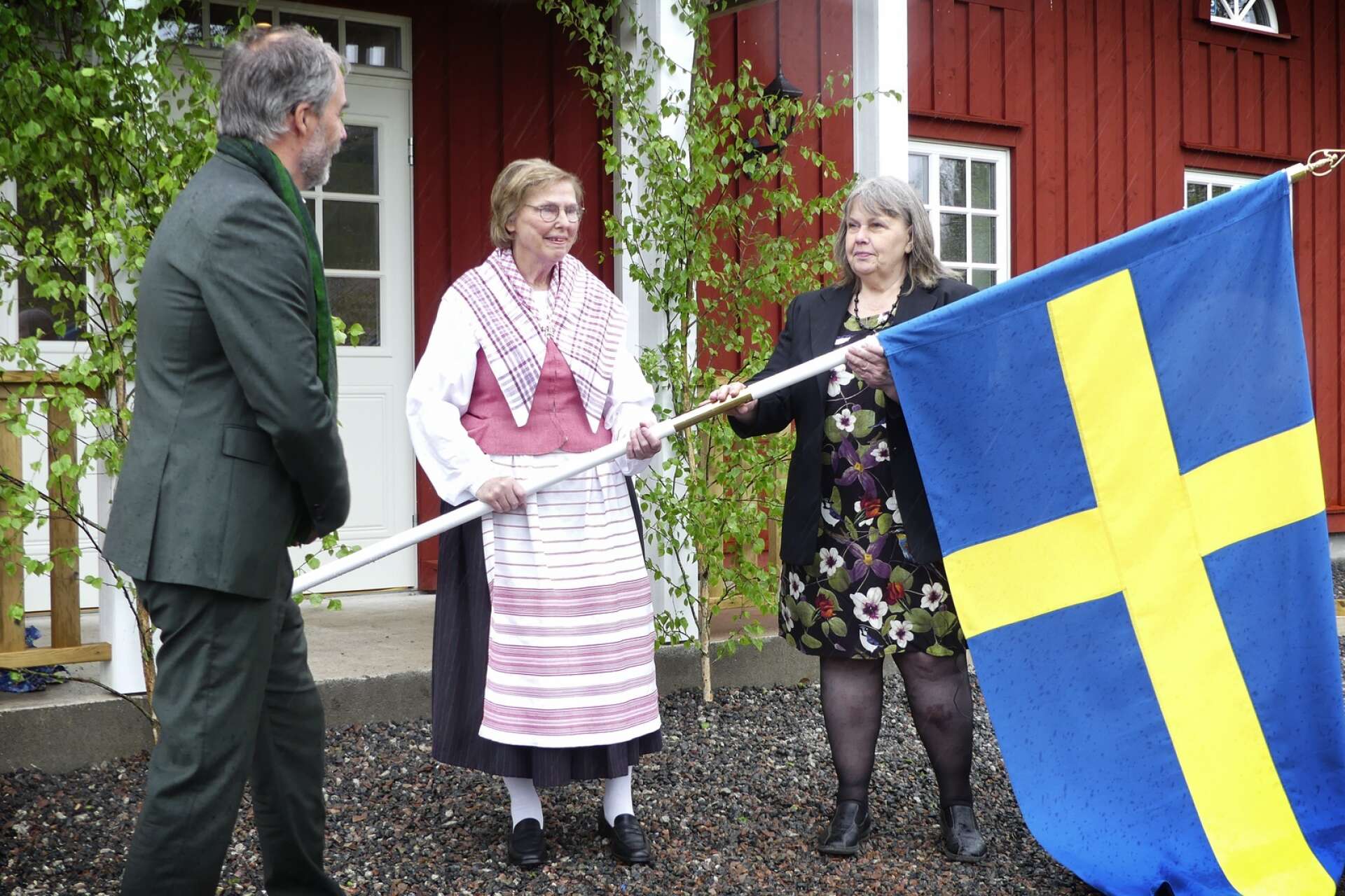 Georg Andrén, landshövding, räcker över fanan till Lena Andersson och Sylvia Nilsson från Svanskogs hembygdsförening.