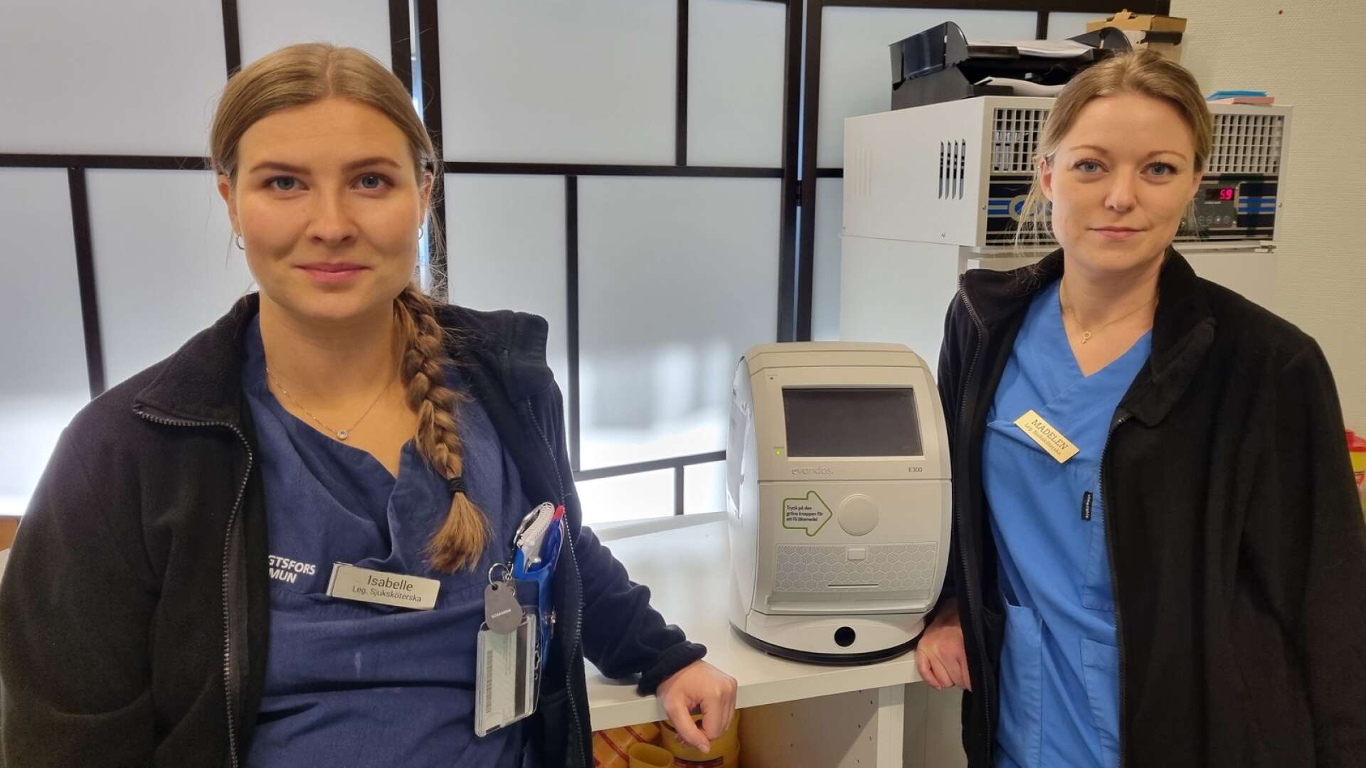 Sjuksköterskorna Isabelle Bloom och Madelen Pettersson vid en av de läkemedelsrobotar som Bengtsfors kommun hyrt in.