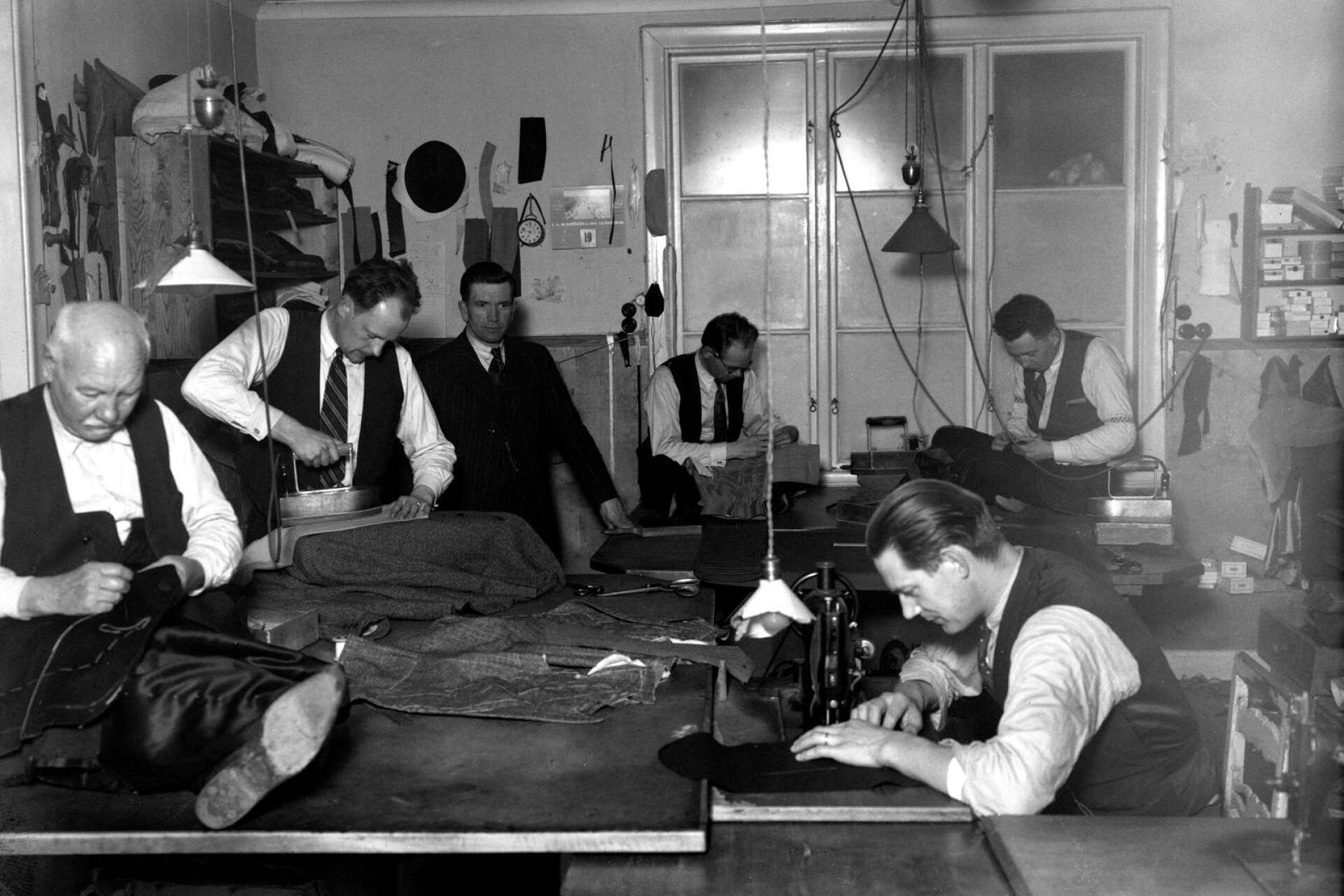 Flitets lampa lyser hos skräddare Lars Holmström och hans kollegor i Filipstad på en bild från 1939. Att lämna in kläder till skräddaren var vanligt under den här tiden.